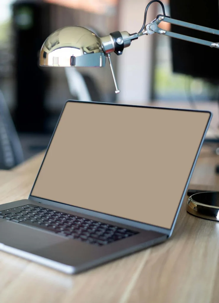 Open laptop with a blank screen on a wooden desk, next to a metallic desk lamp and black smartphone in an office setting, offering the serenity akin to a quiet moment in Christchurch boudoir.