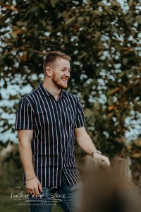 A man wearing a short-sleeved, striped shirt is standing outdoors, smiling, with trees visible in the background—an image that effortlessly captures natural charm and serves as an ideal SEO keyword for your content.