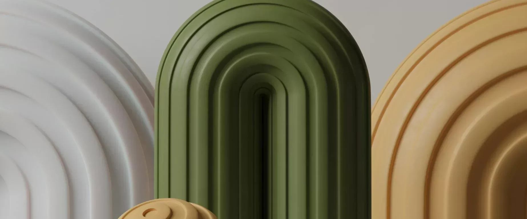 Three arched structures in white, green, and beige stand behind two spherical objects with spiral grooves, one beige and one white, on a plain gray surface.