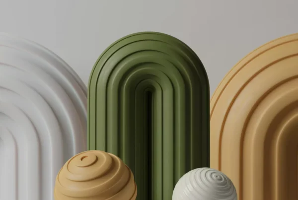 Three arched structures in white, green, and beige stand behind two spherical objects with spiral grooves, one beige and one white, on a plain gray surface.